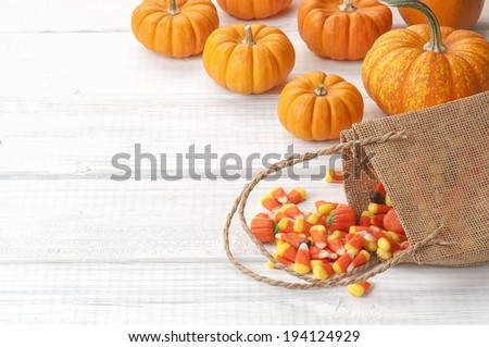 Candy Corn Spilling from Burlap Bag with mini pumpkins on Rustic White or Gray Wood Board Background with room or space for copy, text.  Horizontal