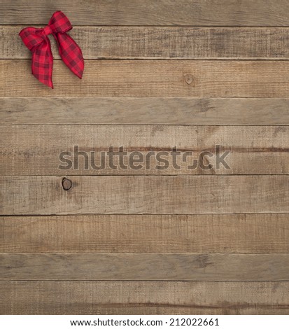 Cute Red Checked Christmas Bow in Upper Corner on Rustic Wood Board Background with Room or space for copy, text, words.  Country style barn look vertical that can be cropped to horizontal