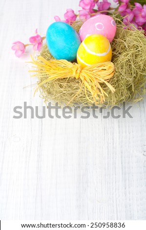 Pretty Easter Eggs in Nest with Pink Flowers in top of framework on Rustic Painted Wood boards with blank, empty room or space for copy, text, your words.  Vertical above view, closeup.