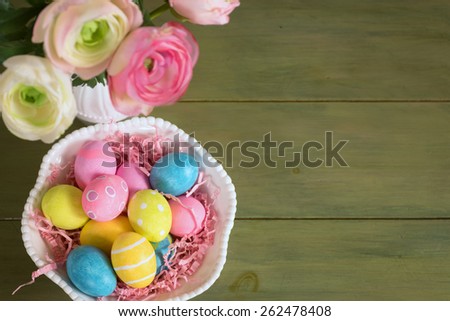 Looking Down on Pretty, Colorful Easter Eggs in a Bowl with Flowers in a Vase on a Rustic Green Painted Wood Board Background with Room or Space for Copy, Text, or Your Words.  Horizontal above view