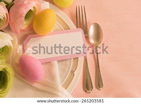 Elegant Peachy Pink Easter Table Place Setting in Warm Light with Two Colorful Dyed Eggs, Flowers, note card.  Background on side for copy, text, your words.  Horizontal above view looking down