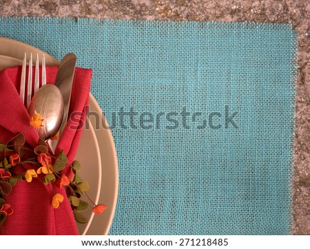 Fall, Summer Placesetting above view with tan plates, fork, knife, spoon, napkin, ring, on cyan burlap placemat on stone table with room or space for copy, text, words.  Horizontal looking down