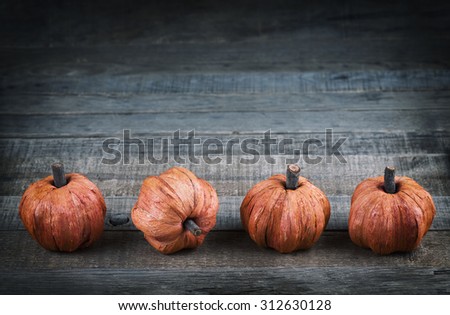 Cute Thanksgiving Mini Pumpkins made of fibers in row at bottom of rustic wood board background with room or space for copy, text, your words. Horizontal dark, cool cross balance tones with vignette