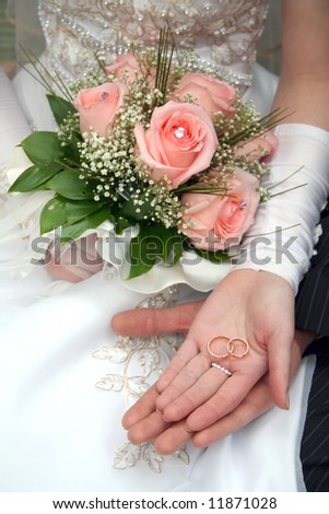 Two rings on palms of a newly-married couple, a bouquet of roses in a hand