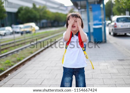 Toddler boy with backpack covered his face with hands at tram stop look like he missed some train or sad. back to school concept