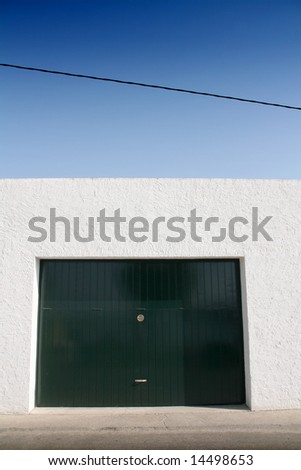 green door garage, white wall and blue sky, sidewalk and street