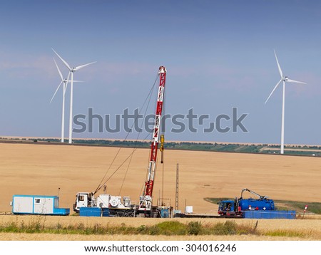 Oil and Gas Drilling Equipments with Wind turbine on background. Exploitation of the two sources of energy.
