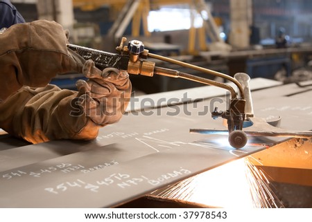 Factory worker cutting metal sheets using acetylene torch