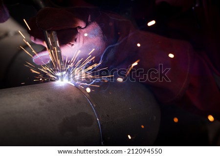 welder in factory with protective equipment welding pipe