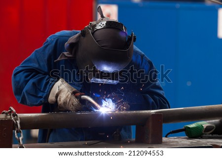 welder in factory with protective equipment welding pipe
