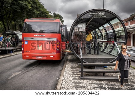 CURITIBA, BRAZIL - MARCH 31: Curitiba's Public Transportation System with its famous red buses and integrated tube-shaped bus stops loading and unloading commuters on March 30, 2014.
