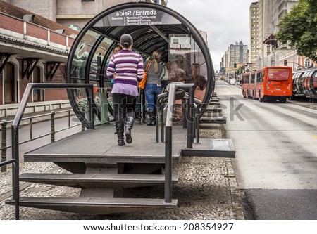 CURITIBA, BRAZIL - MARCH 30 - Public transportation system in Curitiba, PR, Brazil with its famous red buses and tube-shapped bus stops with commuters getting on and out of buses on March 30, 2014.