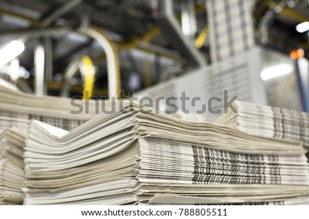 stack of freshly printed daily newspapers transported to a printing plant, in the background machines and technical equipment of a large printing plant