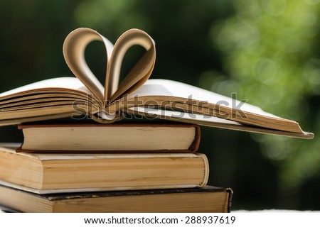 stack of books on table in garden with top one opened and pages forming heart shape