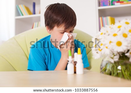 Young boy blowing nose with nazal sprays and other medication in foreground - allergy cocnept