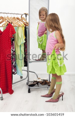 Little girl trying on large shoes standing in front of mirror