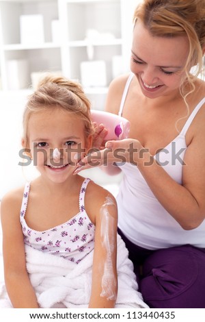Beauty ritual - little girl and mother applying body lotion after bath