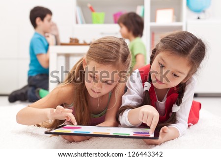 Little girls playing on a tablet computing device - laying on the floor