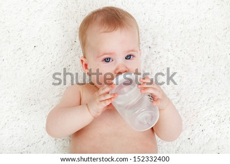 Baby girl drinking water from feeding bottle - laying on white rug