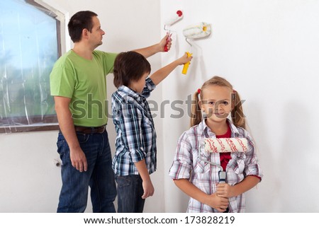 Kids and their father painting a room using paint roller - focus on girl in foreground