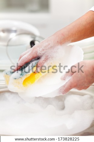 Woman washing the dishes in the kitchen sink area - closeup on hands