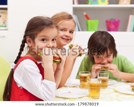 Three kids chomping on healthy sandwiches with cheese and vegetables