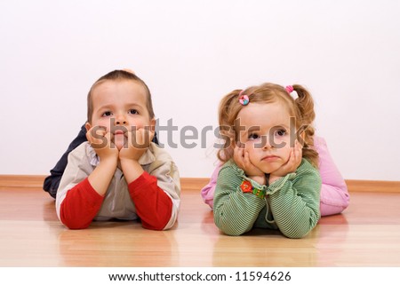 Two kids bored, looking at something - laying on the floor