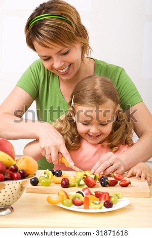 Little girl and her mom having fun preparing summer fruits salad