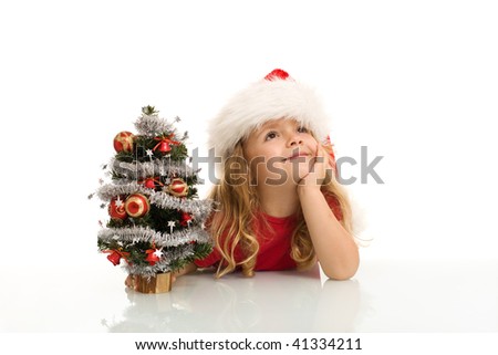 Little girl dreaming of white christmas by a small decorated tree - isolated
