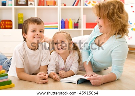 Kids laughing and having fun reading stories with their mother laying on the floor at home