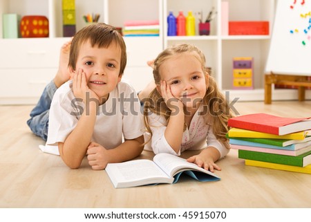 Happy kids with colorful books laying on the floor in their home