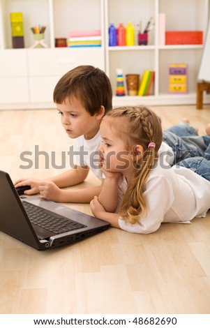 Kids busy and concentrated working on a laptop laying on the floor in their room