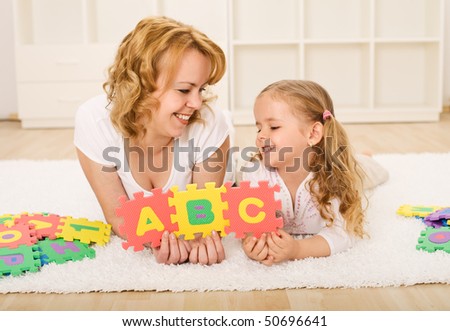 Woman and little girl having fun playing with alphabet puzzle on the floor