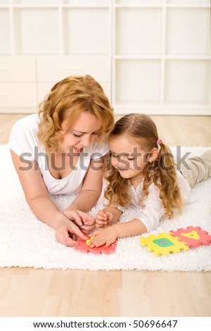 Woman and little girl playing on the floor with alphabet puzzle pieces