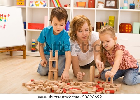 Woman and kids playing with wooden blocks laying on the floor