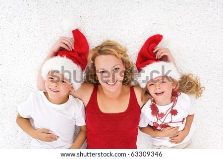 Woman and kids laying on the floor at christmas time wearing santa hats
