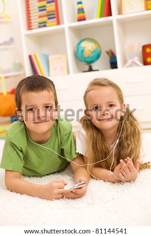 Kids sharing earphones of a music player laying on the floor in their room