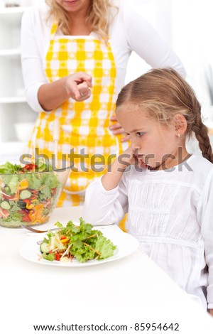 Mother training a healthy eating habit in her child - eating vegetable salad