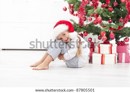 Happy little girl sitting under the christmas tree with presents