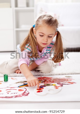 Little girl painting with finger sitting on the floor