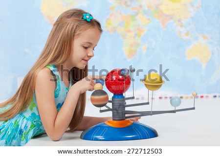 Little girl studies the solar system in geography class - looking at the scale model of planets