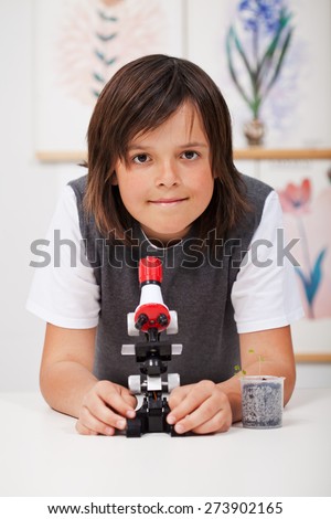 School boy in science class with microscope and young plant - study biology