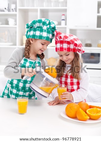 Girls making fresh and healthy orange juice with kitchen appliance