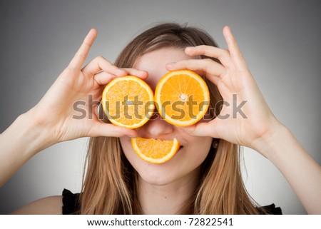 beautiful blond girl using orange as glasses and smiling with a quater orange