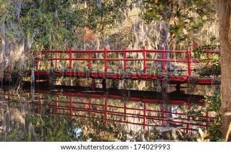 Romantic red bridge in a southern garden under trees covered with hanging moss.