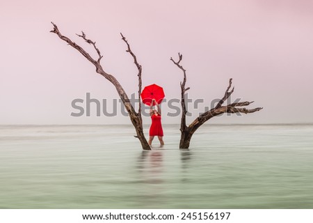 Conceptual image of uncertain victory where a woman in red displays joy and triumph over cancer while her feet sink in the sand.