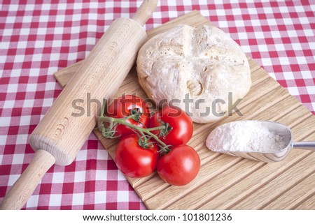 Kitchen still life with tomato, bread and flour on a checkered red table cloth.