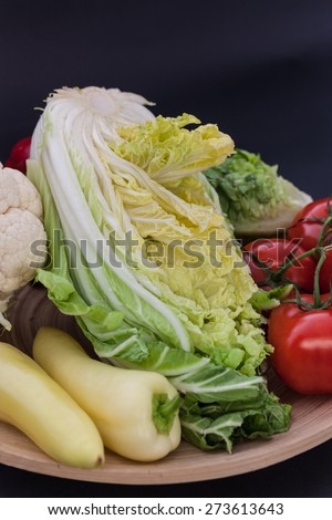 Wooden bowl full of vegetables (cauliflower, yellow peppers, tomatoes, parsley, Chinese cabbage, red bell peppers, cucumber, chives, onions)