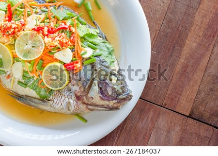 Steamed Nilotica fish,thai style steamed fish in spicy sauce,wood background