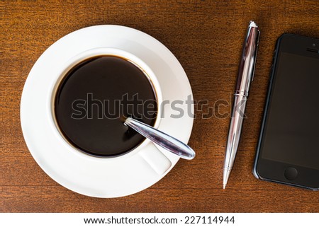 Cell phone and cup of the coffee on the wooden table